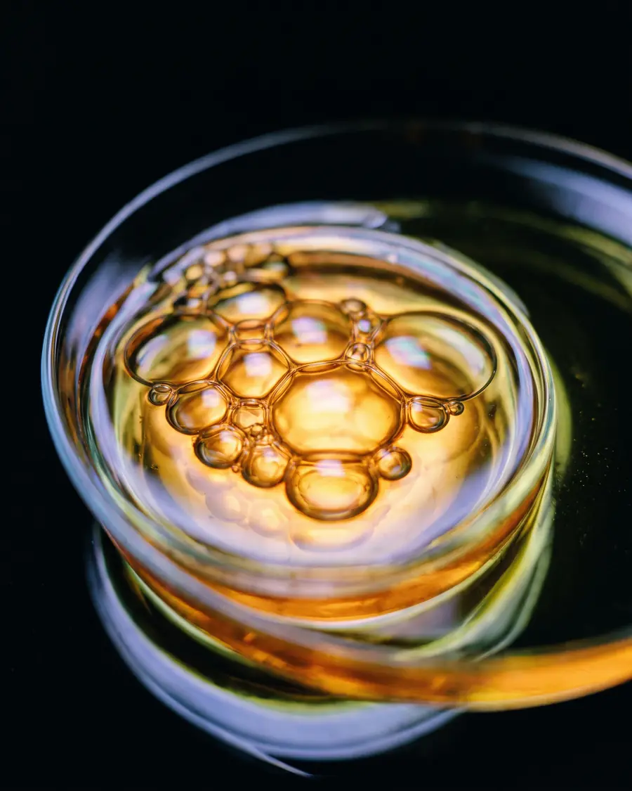 Golden fragrance oil swirling in a glass dish, lit from behind into luminous amber cells